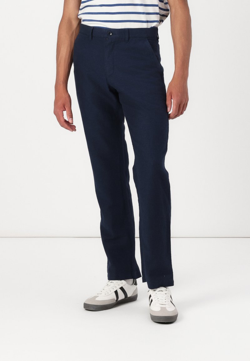 Marineblå bomullsbukser med rett ben-design, med en frontknapplukking og sidelommer, kombinert med hvite joggesko.