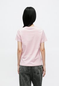 Világos rózsaszín pamut rövid ujjú póló, kerek nyakkivágással és sima textúrával, sötétszürke farmernadrággal párosítva, amely enyhe kopottságot mutat.