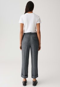 Graue, strukturierte Hose mit weitem Schnitt, umgeschlagenen Bündchen und einer einzelnen Gesäßtasche. Kombiniert mit einem schlichten weißen T-Shirt.