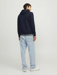 Marinefarbener Hoodie mit weichem Material und geripptem Saum, kombiniert mit hellblauen, locker sitzenden Jeans und weißen Turnschuhen.