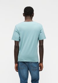 Ανοιχτό γαλάζιο βαμβακερό μπλουζάκι με στρογγυλή λαιμόκοψη και κοντά μανίκια, συνδυασμένο με μπλε τζιν παντελόνι. Απλός σχεδιασμός, ομαλή υφή, χωρίς σχέδια.