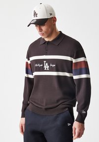 Bruine gebreide polo met witte, bordeauxrode en marineblauwe strepen, met een kraag en knopenlijst; 'Los Angeles Dodgers' logo prominent weergegeven.