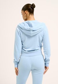 Ljusblå hoodie med dragsko, mjukt tyg och känguruficka. I kombination med matchande tapered byxor. Slät textur, avslappnad design.