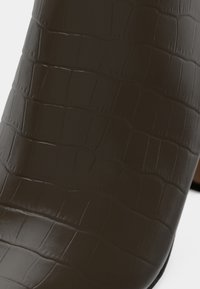 Brune ankelstøvler i kunstskinn med krokodillemønster, med en glatt, blank finish og en avsmalnet silhuett med en svart hæl.