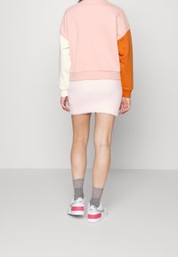 Felpa a blocchi di colore rosa e arancione con maniche bianche, abbinata a una mini gonna pelosa rosa chiaro e sneaker bianche con dettagli rosa.