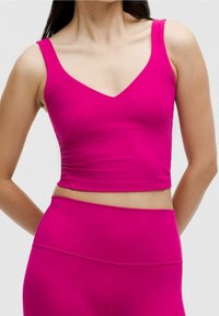 Obcisły crop top w jaskrawym różu. Wykonany z gładkiego, elastycznego materiału z dekoltem w kształcie litery V i szerokimi ramiączkami, odsłaniającym brzuch.