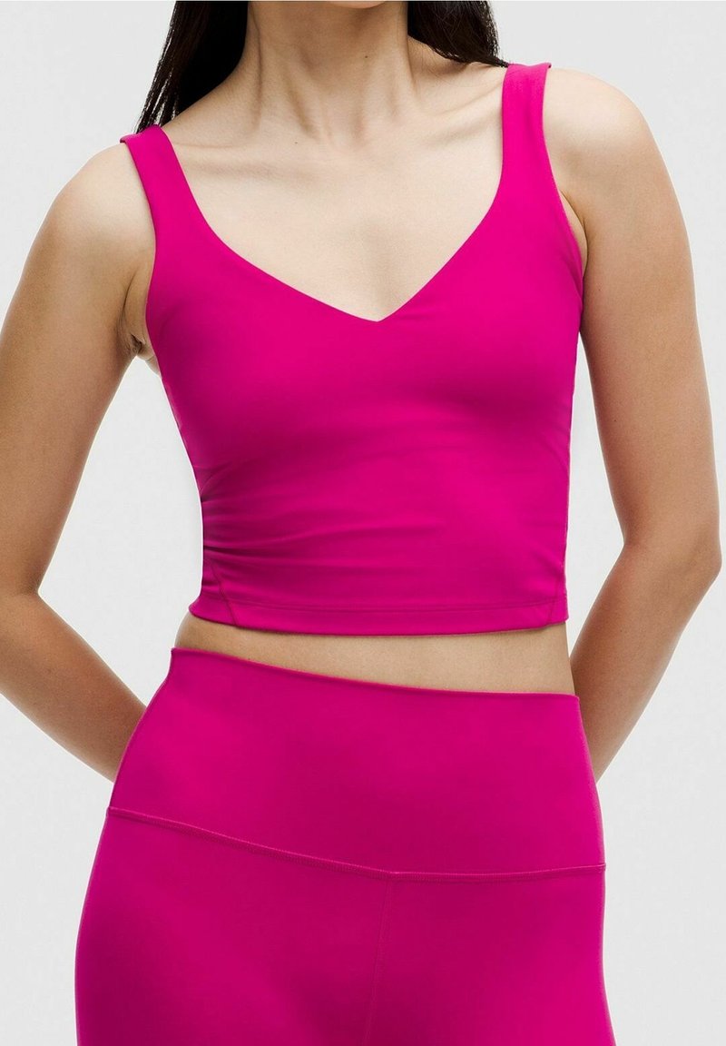 Obcisły crop top w jaskrawym różu. Wykonany z gładkiego, elastycznego materiału z dekoltem w kształcie litery V i szerokimi ramiączkami, odsłaniającym brzuch.