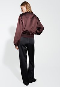 Giacca bomber in satin bordeaux con maniche a palloncino e orlo a costine, abbinata a pantaloni neri a gamba dritta, che mostra un aspetto elegante.