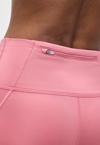 Κοντινό πλάνο της κάτω μέσης ενός ατόμου που φοράει ροζ κολάν με μια μικρή οριζόντια τσέπη με φερμουάρ στη μέση.