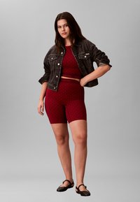 Rød mønstret atletisk top og shorts, lagd med en mørk denimjakke. Glat stof, geometrisk design, parret med brune slip-on sko.