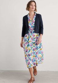 Kratka obleka midi s cvetličnim potiskom in prilegajočim zgornjim delom ter krilom A-linije, s purple, rumenimi in zelenimi vzorci na belem ozadju. Ujemajoča temna kardigan.