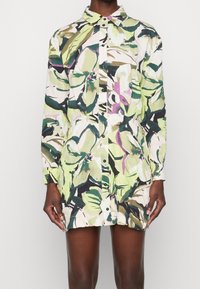 Kukallinen paitamekko vihreän, vaaleanpunaisen ja mustan sävyissä. Varustettu nappisuljenta etuosassa, teräväkauluksella ja pitkillä hihoilla. Rakenne, jossa on karkea kangas ja rento istuvuus.