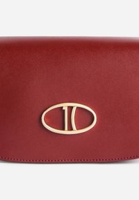 Borsa rossa in pelle con texture liscia, caratterizzata da un dettaglio ovale in metallo dorato con il numero "10". Design compatto, estetica minimalista.