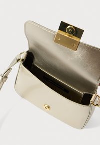 Kremna torbica iz lakiranega usnja z zlatim zaponkom, zlatim okovjem in prostorno notranjostjo. Enostavno nastavljiv nastavljiv naramni trak.