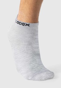 Calcetín de tobillo gris claro, hecho de material suave, con un logo negro en la parte superior. Se ajusta cómodamente alrededor del tobillo.