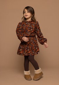 Langdurige mouw, bloemenjurk in donkerbruin, met oranje en witte bloemen. Gecombineerd met bruine leggings en tan laarzen met fleece boorden.