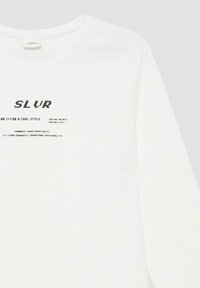 Witte lange mouw shirt met zwarte tekst "SLVR" en zinnen: "Draag het voor een coole stijl," "Verken eindeloze mogelijkheden," en een creativiteit citaat.