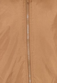 Brun zip-up jakke med en glat, mat tekstur og en central metal lynlås. Enkel design uden yderligere mønstre eller dekorationer.