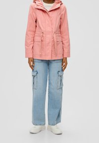 Vaaleanpunainen kevyt takki, jossa on huppu, vyötärö kiristettävissä ja etutaskut; yhdistetty leveälahkeisiin sinisiin cargo-farkkuihin ja valkoisiin lenkkareihin.