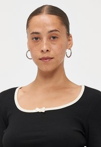 Black long-sleeve top with ribbed texture, rounded neckline, cream ribbed trim, and small cream bow accent at center front.