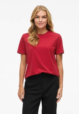 T-shirt rouge à manches courtes et col rond, en tissu doux, avec une coupe droite et une coupe décontractée, associé à un pantalon noir.