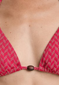 Rdeč bikini vrh s triangularnimi skodelicami in teksturirano tkanino, s lesenim dodatkom na sredini.