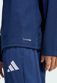 Μπλούζα αθλητικών επιδόσεων σε ναυτικό μπλε χρώμα με το λογότυπο ClimaCool, συνδυασμένη με παντελόνια σε αντίστοιχο χρώμα που διαθέτουν λευκό λογότυπο Adidas, κατασκευασμένα από αναπνεύσιμο ύφασμα.