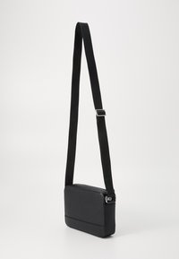 Sac bandoulière en matériau texturé noir avec une forme rectangulaire, doté d'une sangle ajustable et d'accents en métal argenté.