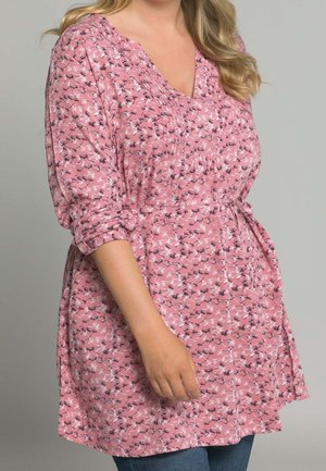 Tunique rose présentant un motif floral avec des accents noirs, décolleté en V, détails froncés sur la poitrine et manches trois-quarts.