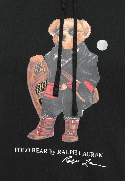 Medvěd s teddy stylem v slunečních brýlích, černé bundě a červených botách, nese sněžnice; text "POLO BEAR od RALPH LAUREN" níže.