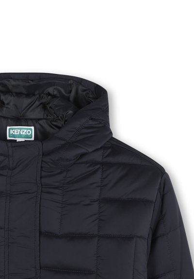Close-up of a dark navy puffer jacket with a high collar, featuring a Kenzo Kids label. The fabric has a quilted texture.