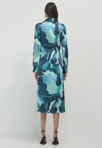 Robe à manches longues en tissu bleu-vert brillant, dotée d'une taille ceinturée, d'un motif abstrait et d'une longueur midi. Col ouvert et poignets boutonnés.