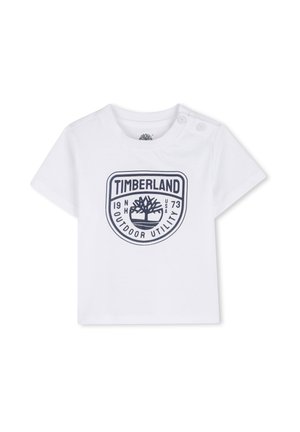 Weißes T-Shirt mit kurzen Ärmeln aus Baumwolle, mit einem dunkelblauen Timberland-Logo, auf dem "OUTDOOR UTILITY" und das Gründungsjahr aufgedruckt sind. Zwei Druckknöpfe an der Schulter.