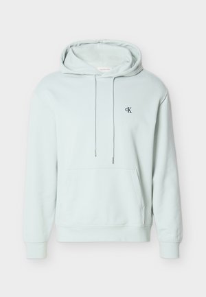 Sudadera con capucha de color azul claro con bolsillo frontal, cordones y un pequeño logo negro "cK" en el pecho izquierdo.