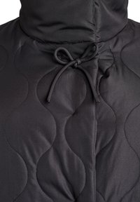 Čierna prešívaná bunda s vysokým golierom, sťahovaním na šnúrku a textúrovaným vlnkovým vzorom na látke. Hladký, ľahký materiál.
