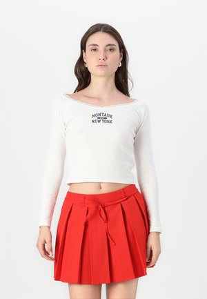 Bijela bluza dugih rukava s čipkastim rubom, s natpisom "Montauk 1975 New York"; uparena s naboranom crvenom suknjom s vezanjem u struku.