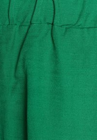 Tissu vert texturé avec un motif tissé, présentant des sections froncées et une finition lisse. Idéal pour les vêtements décontractés ou les superpositions.