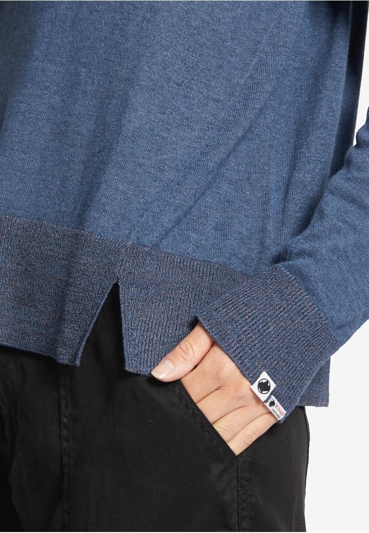 Gestickter blauer Pullover mit kontrastierendem dunklen Saum, der seitliche Schlitze und ein Etikett an der Manschette hat. Weicher Stoff und lässige Passform.