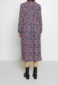 Lång, marinblå klänning med rosa blommönster, rynkad midja, långa ärmar och volangkant. Matchad med svarta ankelstövlar.