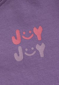 Lila Stoff mit zwei "JOY"-Texten, wobei jeder Buchstabe mit smiley Gesichtern und Herzformen in Rosa und Helllila gestaltet ist.