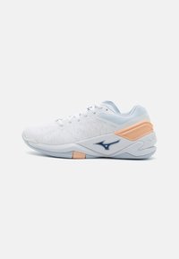 Baskets de sport blanches avec une tige en mesh texturé, accents bleus et contrefort de talon pêche. Dispose d'un laçage à l'avant et d'une semelle rembourrée.
