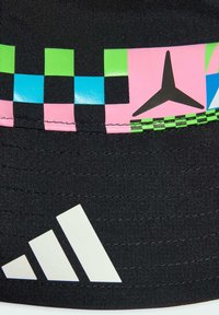 Tela negra con banda de tablero de ajedrez multicolor en verde, azul y rosa, con una estrella de tres puntas y el logo blanco de Adidas en la parte inferior izquierda.