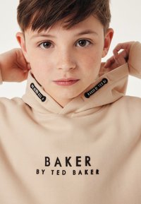 Béžová mikina s kapucí s černým nápisem "BAKER BY TED BAKER" u výstřihu, jemná textura a šňůrková kapuce.
