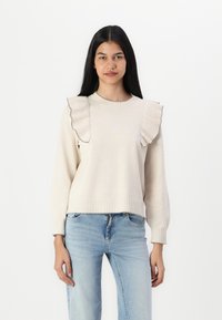 Lys beige genser med rynkede detaljer på skuldrene, ribbede mansjetter og hem. Myk tekstur, rund utringning og avslappet passform.