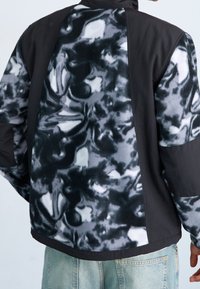 Chaqueta negra y gris con una parte trasera de forro polar de patrón abstracto y suave tela en el frente. Ajuste oversized con un cuello alto.