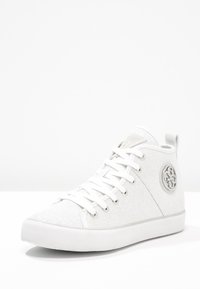 Białe wysokie trampki wykonane z teksturowanej tkaniny, z okrągłym metalowym logo po boku. Posiadają białe sznurowadła i gumową podeszwę.
