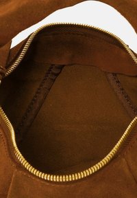 Binnenkant van een bruine suède handtas met een gouden rits, met een gladde textuur en een ruime hoofdcompartiment zonder extra vakken.