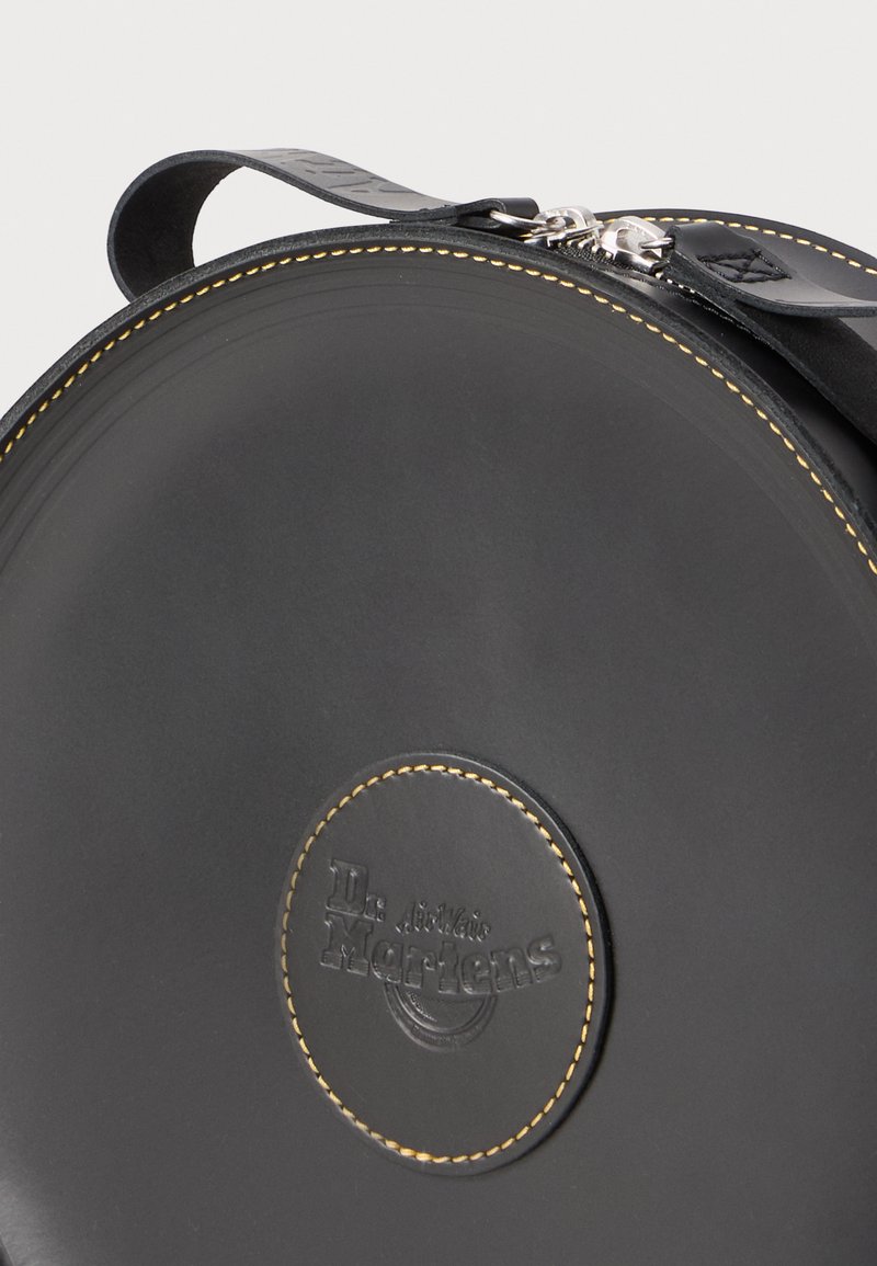 Borsa circolare in pelle nera con cuciture gialle, dotata di un logo in rilievo ben visibile. Include un manico corto e una chiusura a zip.