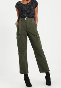 Olivek z cargo w kolorze oliwkowym z wysokim stanem, dużymi bocznymi kieszeniami i materiałowym paskiem z okrągłą klamrą, zestawione z czarną bluzką w groszki.