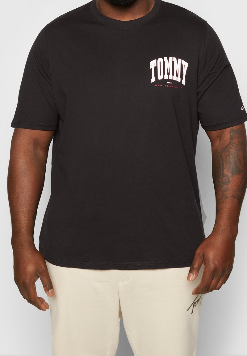 Camiseta de algodón negra con mangas cortas y cuello redondo. Presenta el texto "TOMMY" en blanco y rojo en el área del pecho izquierdo.